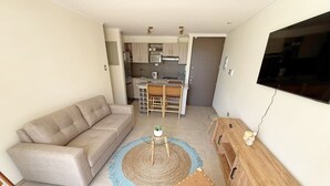 A living room with a sofa, a coffee table, a TV, and a kitchen in the background. - Your Perfect Getaway in La Serena! (La Serena)