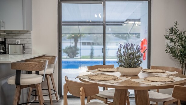 Eine moderne Küche mit Essbereich, einem großen Fenster und Blick auf einen Swimmingpool.