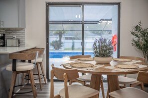 A modern kitchen with a dining area, a large window, and a view of a swimming pool.