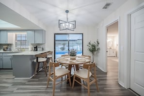 Una cocina moderna con una isla central, mesa de comedor y sillas, un amplio ventanal y vistas al exterior.