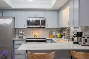 A modern kitchen with grey cabinets, a stainless steel refrigerator, a microwave, and a coffee maker.