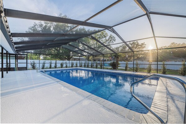 A swimming pool with a glass enclosure, surrounded by a white deck and metal railings.