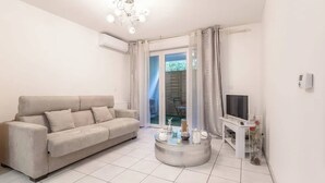 A living room with a sofa, a coffee table, a TV, and a sliding glass door leading to an outdoor area. - T2 -  Cocon du Lancier - Terrasse et Parking (Marseille)