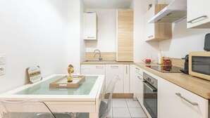 A modern kitchen with white cabinets, a wooden countertop, a microwave, and a glass-top dining table. - T2 -  Cocon du Lancier - Terrasse et Parking (Marseille)