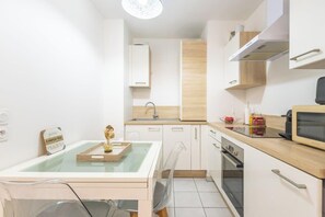 Une cuisine moderne avec des meubles blancs, un plan de travail en bois, un four à micro-ondes et une table à manger avec un plateau en verre.