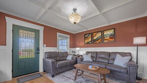 Un salon avec deux canapés gris, une table basse en bois, une porte verte avec une fenêtre et un luminaire au plafond.