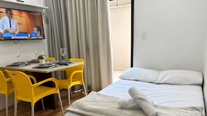 Una habitación de hotel con cama, escritorio con sillas, televisor y ventana con cortinas.