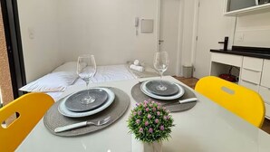 Un rincón comedor con una mesa lista para dos personas, una pequeña planta en maceta y una puerta blanca al fondo.