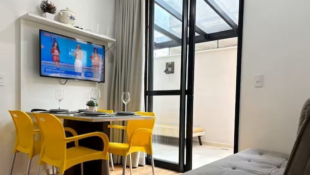 Una habitación moderna con zona de comedor, sofá y televisor montado en la pared.