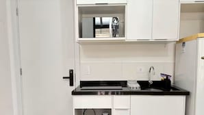 Una cocina compacta con armarios blancos, encimera negra y un electrodoméstico rojo.