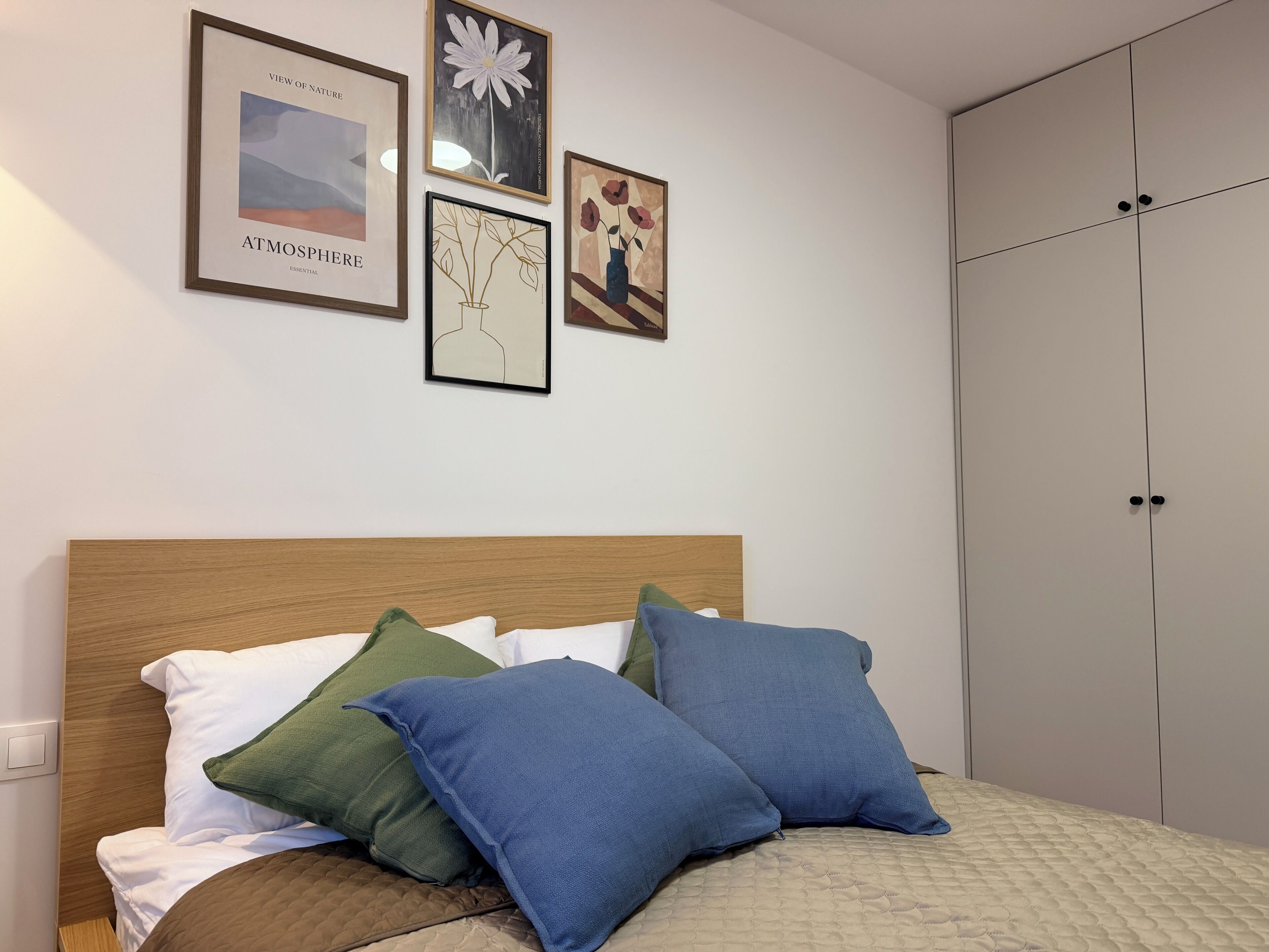 Een slaapkamer met een houten hoofdbord, een bed met witte en blauwe kussens, en een garderobe met twee deuren.