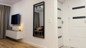 A modern hotel room with a flat-screen TV, a large mirror, a bedside table with a lamp, a chair, and a wardrobe. - Modern Apartment PKiN Best Location (Warsaw)
