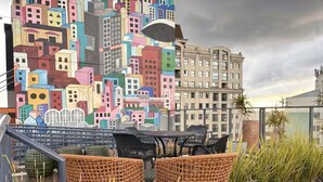 A rooftop terrace with wicker chairs, a table, and a cityscape mural. - Studio in the city center | Near Passeio Público (Curitiba)