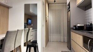 A modern kitchen with a built-in oven, a microwave, and a coffee machine. There is a dining area with chairs and a table. - Studio in the city center | Near Passeio Público (Curitiba)