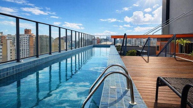 A rooftop pool with a clear view of the city skyline, a wooden deck, and a metal railing. - Studio in the city center | Near Passeio Público (Curitiba)