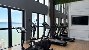 A gym with treadmills, an elliptical, and a TV on a white wall. - Apartment with gym, terrace, pool and sea view. (Itapema)