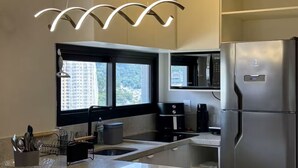A modern kitchen with a stainless steel refrigerator, a built-in oven, and a microwave. There is a window providing a view of the outside. - Apartment with gym, terrace, pool and sea view. (Itapema)