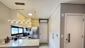 A modern kitchen with a central island, built-in appliances, and a large window. - Apartment with gym, terrace, pool and sea view. (Itapema)