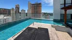 Una piscina en la azotea con vistas a la ciudad, una terraza de madera y una fachada de edificio moderna.