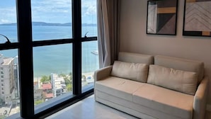Una habitación con un gran ventanal, un sofá color crema y dos cuadros enmarcados en la pared.