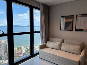 Ein Zimmer mit großem Fenster, einem beigen Sofa und zwei gerahmten Kunstwerken an der Wand.