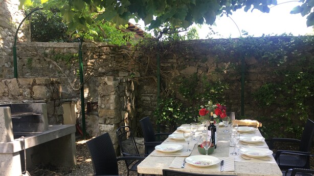 An outdoor dining area with a stone wall, a grill, and black wicker chairs. - ANCIENT HOUSE OF NEL CHIANTI FOR 10 PEOPLE (Toscana)