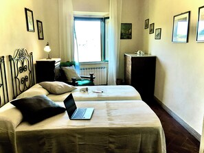 Ein Zimmer mit einem Bett, einem Laptop, einem Schminktisch, einem Fenster und mehreren gerahmten Bildern an den Wänden.
