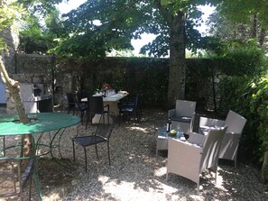 Eine Terrasse im Freien mit einer Steinsäule, einem Esstisch, Korbstühlen und einem Grill.