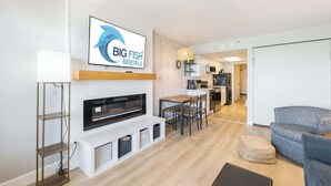 Una sala moderna con chimenea, televisor montado en la pared, comedor y cocina al fondo.