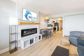 A modern living room with a fireplace, a television mounted on the wall, a dining area, and a kitchen in the background. - Beautiful Unit with Direct Oceanfront Views & Pool (Myrtle Beach)