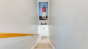 Een trap die leidt naar een deur, boven de deur hangt een foto van een vuurtoren in een lijst.