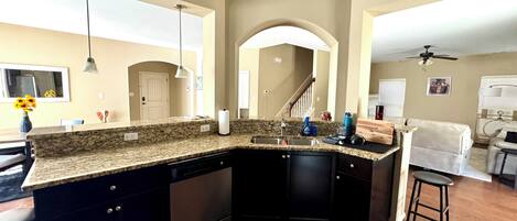 A kitchen with a granite countertop, black cabinets, a dishwasher, and a sink.