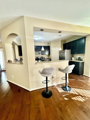 A modern kitchen with dark cabinets, a central island, and two bar stools. - Masters Week Rental Gem-10mins to Augusta National/3BR MordenHome (Augusta)