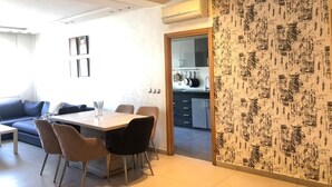 Una sala de estar moderna con comedor, y una cocina visible a través de una puerta abierta, con una pared decorada con un diseño.