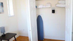 A room with a wooden floor, a closed door, a window, and a closet with folded towels and a blue ironing board. - Beautiful 1Bed 1 Bath w/ Parking (Belleville)