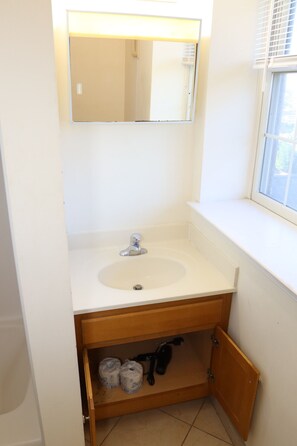 Une salle de bain avec un lavabo blanc, un miroir et une fenêtre.