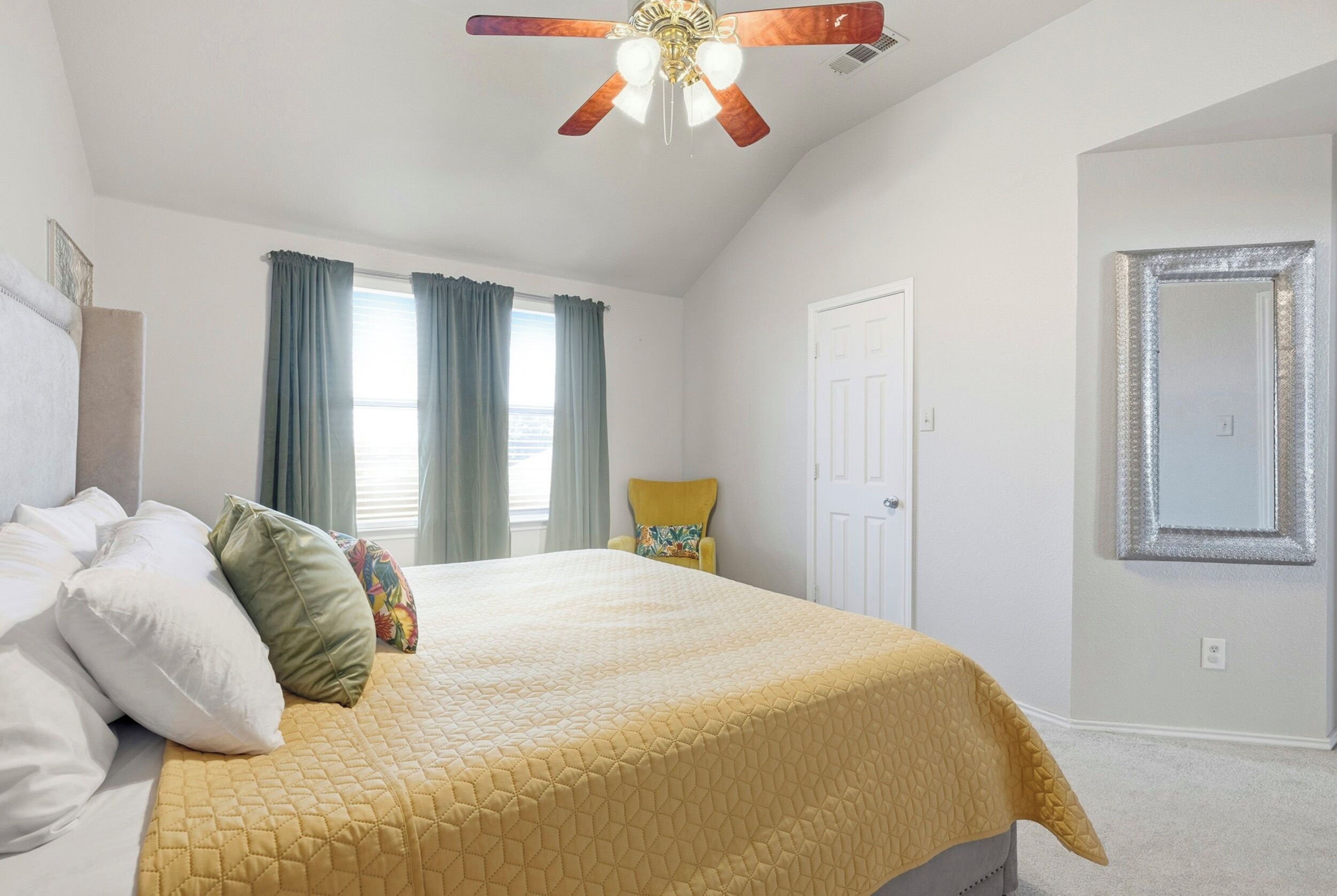A bedroom with a bed, a ceiling fan, a window with curtains, and a door.