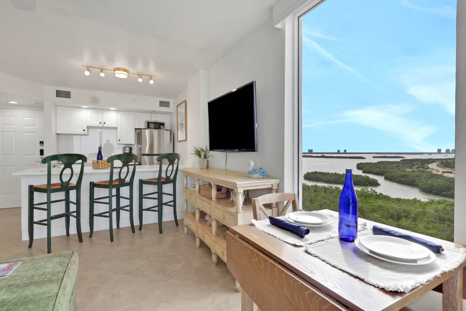 Una cocina moderna con armarios blancos, un refrigerador de acero inoxidable y un televisor de pantalla plana.