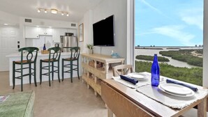 Ett modernt kök med vita skåp, ett kylskåp i rostfritt stål och en platt-TV.
