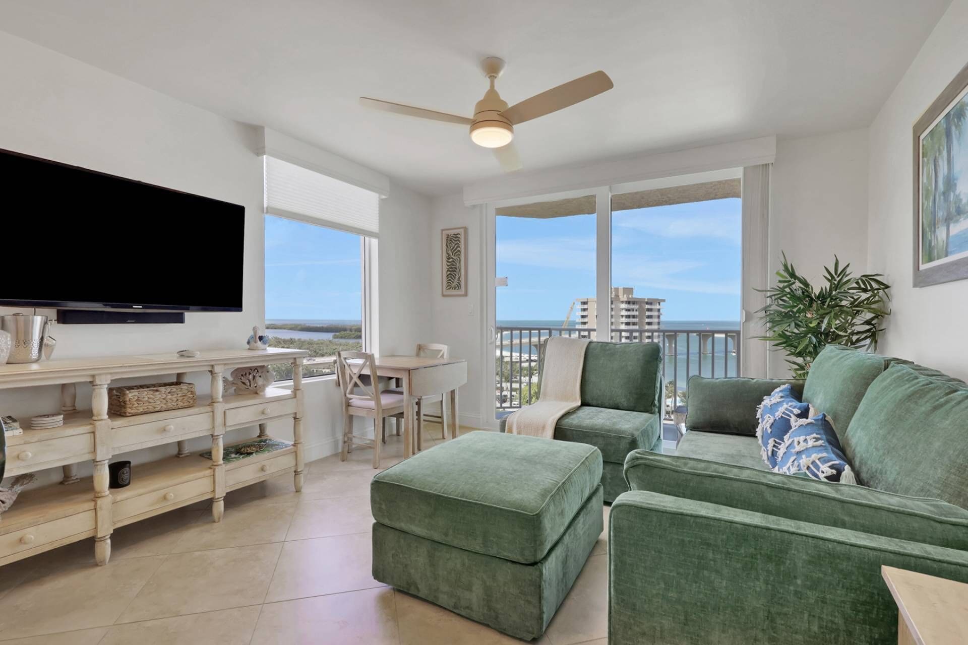A spacious living area with a flat-screen TV, a ceiling fan, a dining table, and a green sofa.