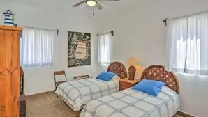 A bedroom with two beds, a ceiling fan, a painting, and a window with curtains.