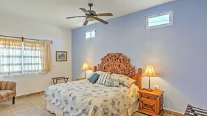 Een slaapkamer met een bed, twee bedlampen, een plafondventilator, een raam met gordijnen en een klein tafeltje.