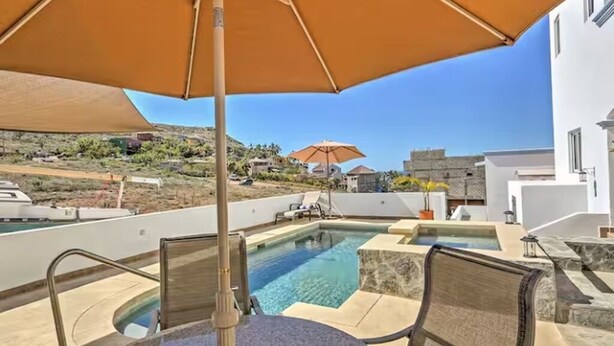 A swimming pool with a sun umbrella, lounge chairs, and a view of a hillside.