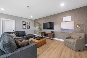 A modern living room with a grey sectional sofa, a wooden coffee table, a TV on the wall, and a small side table.