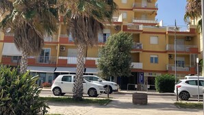 A multi-story residential building with balconies, parked cars, and palm trees. - Spacious 3-bedroom beachfront apartment (Pozzallo)