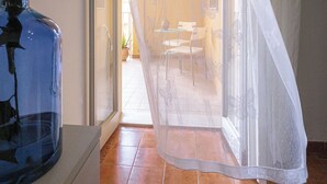 A room with a tiled floor, a table with chairs, a potted plant, and a window with a curtain. - Spacious 3-bedroom beachfront apartment (Pozzallo)