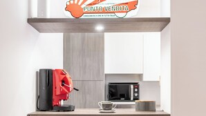 A compact kitchen with a microwave, coffee machine, and a red table with a golden decorative item. - Spacious 3-bedroom beachfront apartment (Pozzallo)
