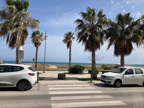 A parking area with white cars, palm trees, and a beach in the background.