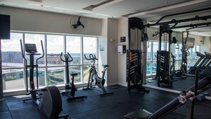 Ein Fitnessstudio mit unterschiedlichen Trainingsgeräten, großen Fenstern und Blick auf die Stadt.