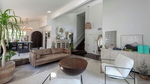 Ein geräumiges Wohnzimmer mit Sofa, Couchtisch und Sesseln, einer Treppe zu einer weiteren Ebene sowie einem Essbereich mit Tisch und Stühlen.